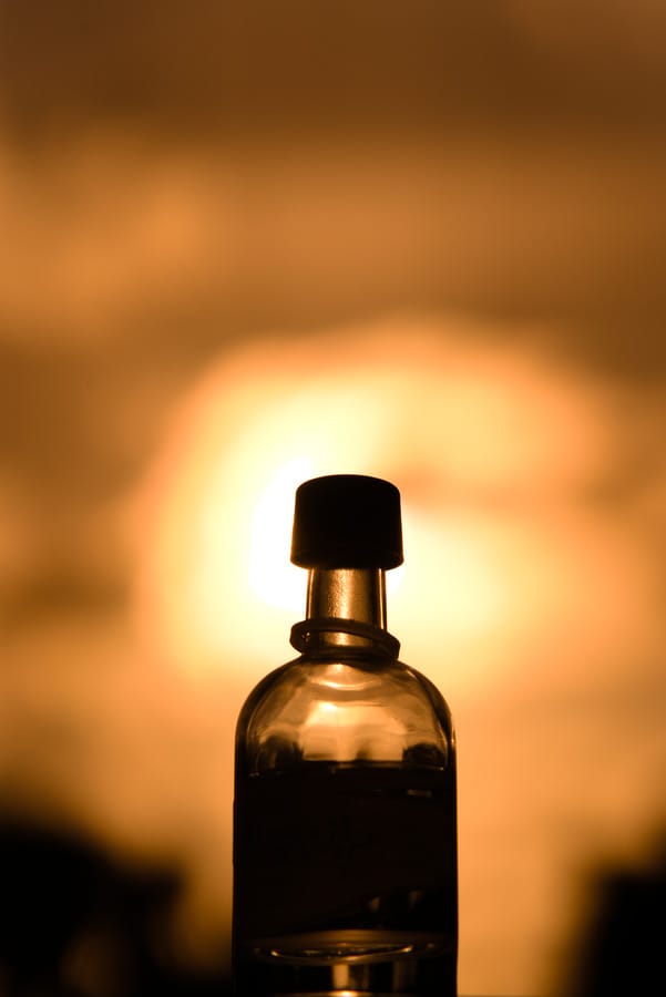 Silhouetted glass bottle photographed against a glowing sunset sky, with warm yellow and orange tones from creative white balance editing.